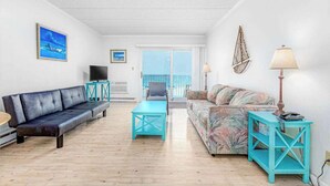 A living room with a sofa, a coffee table, a TV, and a balcony with a view. - Barefoot Country 303 (Ocean City)