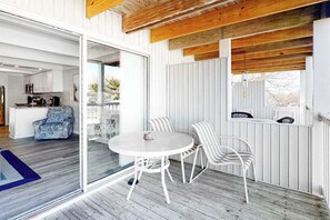 A modern interior with a dining area featuring a round table and white chairs, a kitchen visible through an open door, and a wooden ceiling. - Beachwalk 23 (Ocean City)