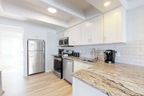Cocina moderna con armarios blancos, electrodomésticos de acero inoxidable, encimera de granito y piso de madera.