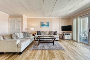 A living room with a sofa, coffee table, TV, and a painting on the wall. - White Marlin 209B (Ocean City)
