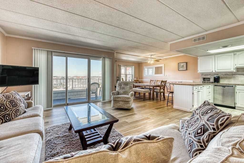 A spacious living area with a sofa, armchair, and coffee table, a dining area with a table and chairs, and a kitchen with cabinets and a countertop.