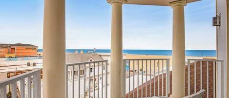 A balcony with two chairs, a view of the beach, and a building in the background.