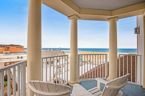 Ein Balkon mit zwei Stühlen und Blick auf den Strand, mit einem Gebäude im Hintergrund.