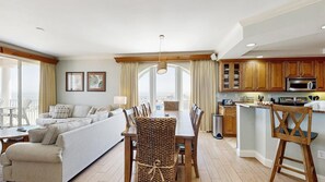 Amplia sala de estar con sofá, mesa de comedor y sillas, cocina con armarios de madera y electrodomésticos, y un balcón con vistas.