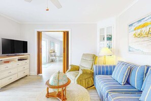 A living room with a TV, sofa, armchair, lamp, globe, and a painting. - Canalfront House w/ Private Deck, Central AC, Free WiFi, Bay Views, Washer/Dryer (Ocean City)