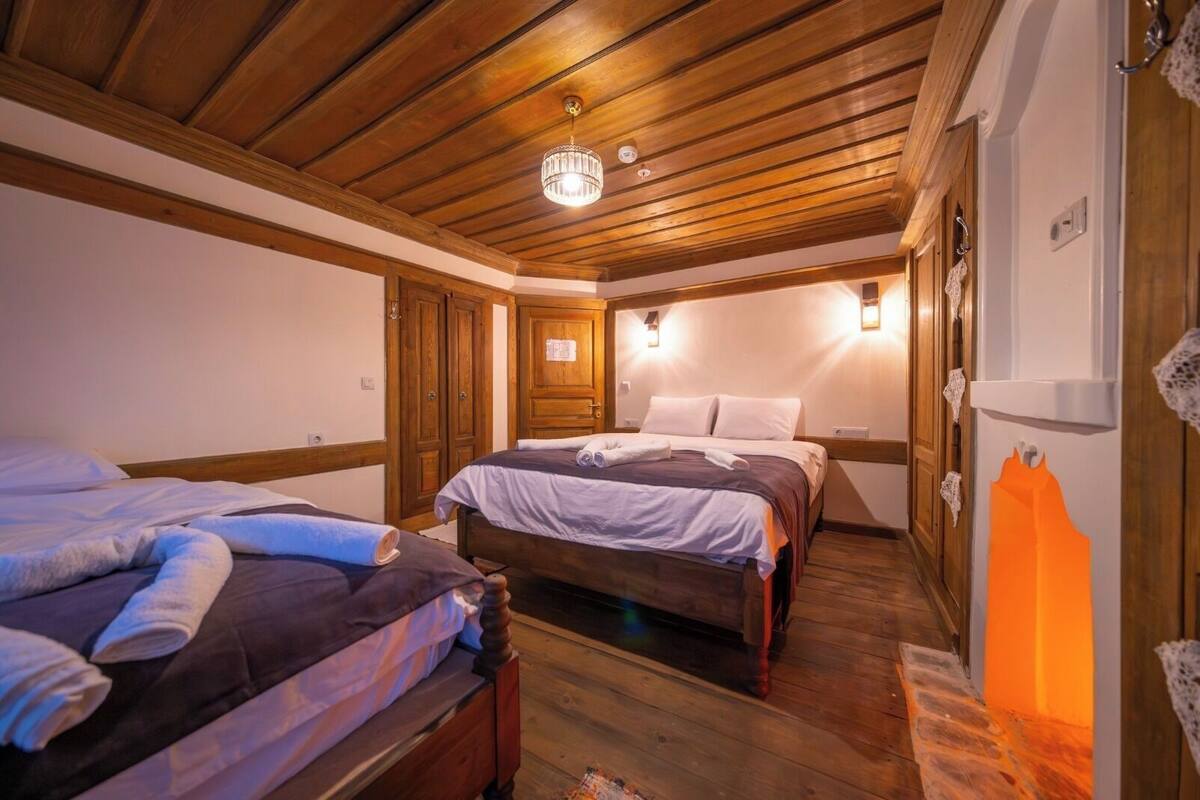 Quarto com tetos de madeira, duas camas, um guarda-roupa de madeira e luminária fixada na parede.