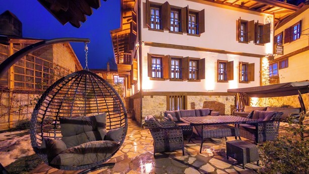 A stone patio with outdoor furniture, a hanging chair, and a building with multiple windows and balconies.