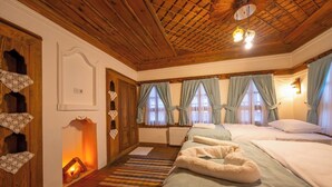 A cozy hotel room with wooden ceilings, a fireplace, a bed with a fluffy white blanket, and a window with curtains.