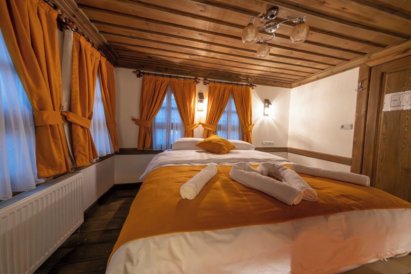 Ein Hotelzimmer mit Bett, Vorhängen, Heizkörper und Deckenleuchte.