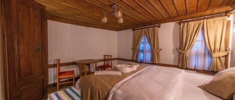 A wooden-paneled bedroom with a bed, two chairs, a small table, and a window with curtains.