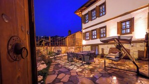 A stone patio with outdoor furniture, a hanging chair, and a staircase leading to an upper level.