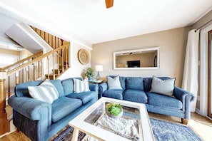 Ein Wohnzimmer mit blauem Sofa, einem Couchtisch mit Pflanze, einer Holztreppe und einem großen Spiegel an der Wand.