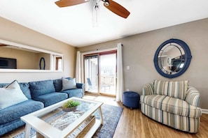 Ein Wohnzimmer mit einem blauen Sofa, einem gestreiften Sofa, einem Couchtisch, einem Deckenventilator und einem großen Spiegel.