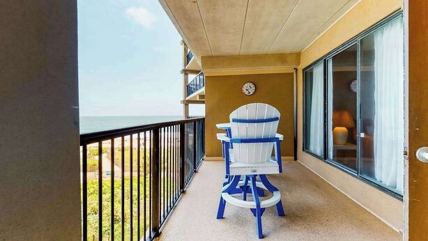 Ein Balkon mit Blick auf das Meer, eine Wanduhr und ein Stuhl.