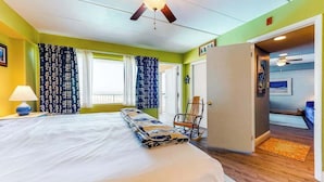 Ein Schlafzimmer mit einem Bett, einem Deckenventilator, einem Sessel und einer Tür zu einem anderen Raum.