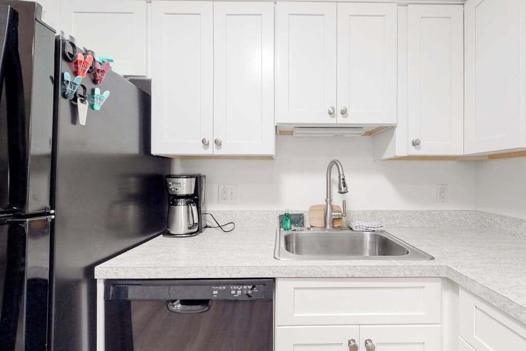 A kitchen with white cabinets, a black refrigerator, a stainless steel sink, and a dishwasher.