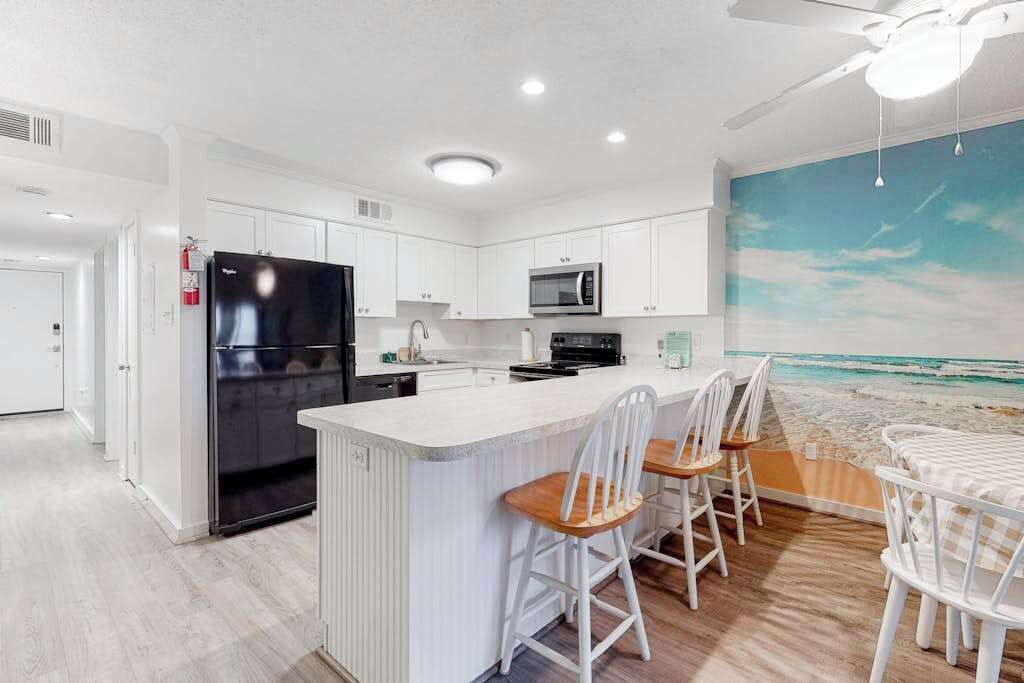 Una cocina moderna con armarios blancos, un refrigerador negro, un microondas y un comedor con sillas y una mesa blancos.