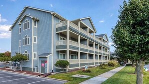 A multi-story hotel with a blue exterior, a parking lot, and a sidewalk. - Baywatch I - 201B (Ocean City)