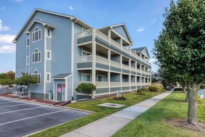 A multi-story hotel with a blue exterior, a parking lot, and a sidewalk. - Baywatch I - 201B (Ocean City)