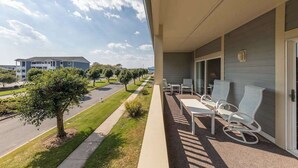 A balcony with outdoor seating, a clear view of a road and trees, and a building in the background. - Baywatch I - 201B (Ocean City)