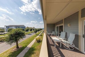 A balcony with outdoor seating, a clear view of a road and trees, and a building in the background. - Baywatch I - 201B (Ocean City)