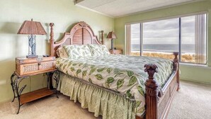 A bedroom with a large bed, two bedside tables, a nightstand, a ceiling fan, and a large window with a view. - Anchorage  304 (Ocean City)