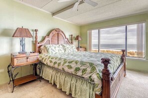 Een slaapkamer met een groot bed, twee nachtkastjes, een ventilator in het plafond en een groot raam met uitzicht.