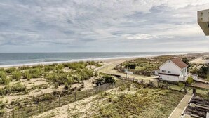 A coastal view with a beach, grassy dunes, and a white house with a red roof. - Anchorage  304 (Ocean City)