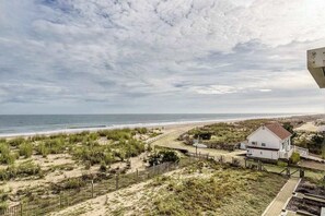 Uitzicht op de kust met een strand, grasduinen en een wit huis met een rood dak.