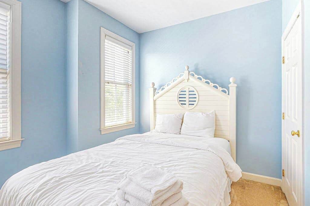 Een slaapkamer met een wit bed, een raam met zonwering en een deur met gouden handvat.