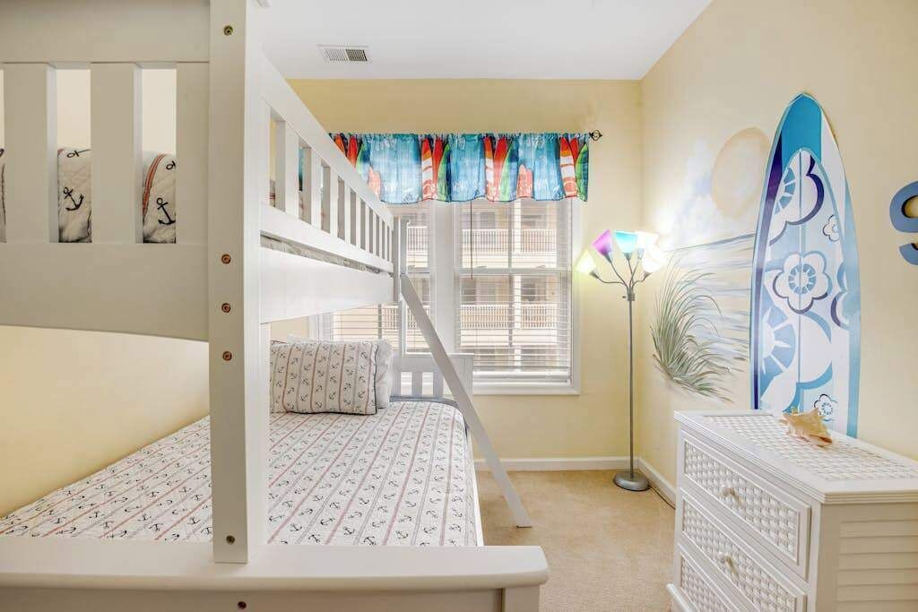 A bedroom with bunk beds, a window with curtains, a surfboard decoration, and a floor lamp.