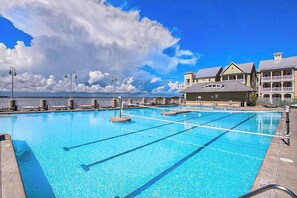 Ein Schwimmbecken mit klarem, blauem Wasser, ein Rettungsturm und im Hintergrund ein Gebäude mit Balkonen.