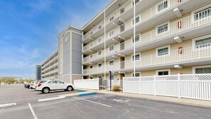 A multi-story residential building with a parking lot, white fences, and a clear sky. - Thunder Island 34B Bay views at Convention Center (Ocean City)