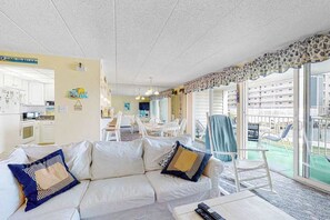 Een woonkamer met een bank, een eethoek en een balkon met uitzicht op gebouwen.