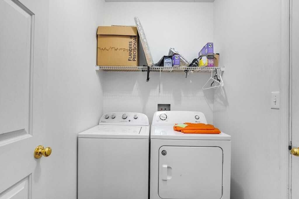 A laundry room with a washing machine, dryer, and a shelf above holding various items.
