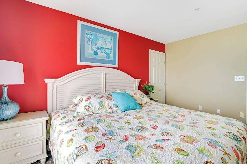 Une chambre avec un lit blanc, un mur rouge et un oreiller bleu.