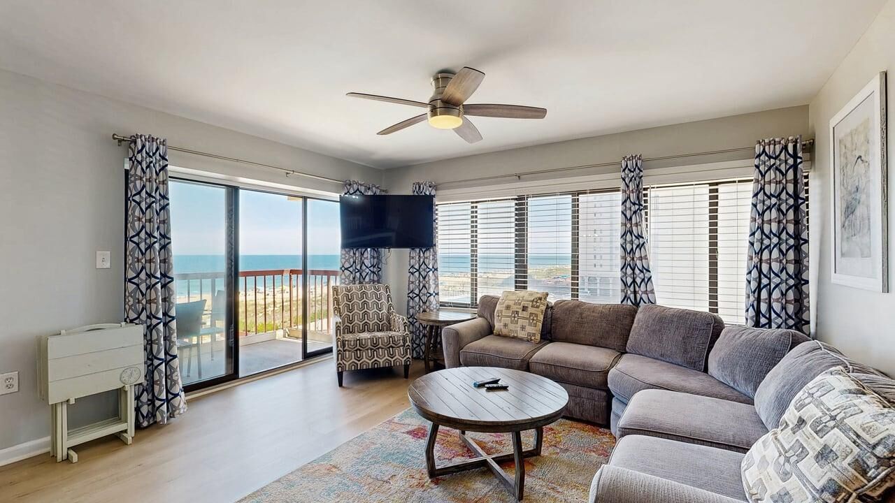 Ein Wohnzimmer mit einer Couch, einem Couchtisch, einem Fernseher und einem Balkon mit Blick auf das Meer.