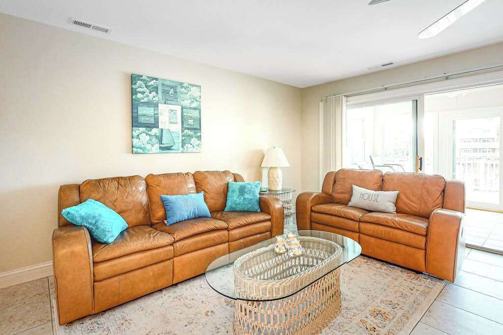 A living room with two brown leather sofas, a glass coffee table, a wall-mounted painting, and a large window.