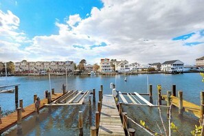 A waterfront dock with wooden planks and posts, a marina with boats, and residential buildings in the background. - Sunset Harbour townhouse with balcony, & central AC (Ocean City)