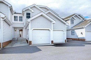 A residential building with a central entrance, two garages, and a brick foundation. - Sunset Harbour townhouse with balcony, & central AC (Ocean City)