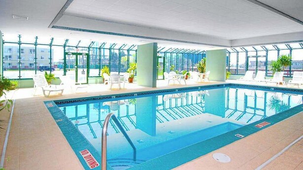 Una piscina interna con pareti di vetro trasparenti, poltrone da relax bianche e piante in vaso.