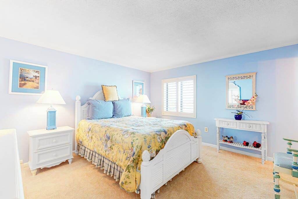 A bedroom with a bed, nightstands, a dresser, a console table, and a window with shutters.