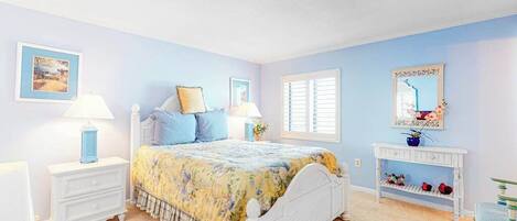 A bedroom with a bed, nightstands, a dresser, a console table, and a window with shutters.