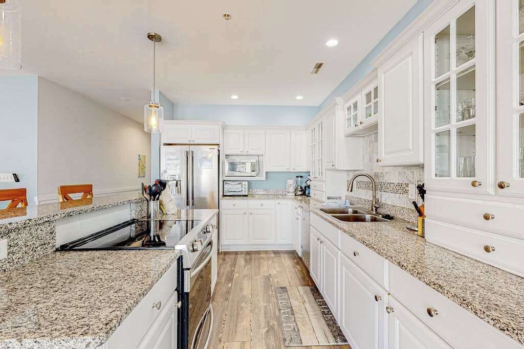 A kitchen with white cabinets, granite countertops, a stainless steel refrigerator, and a built-in microwave.