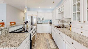 Una cocina con armarios blancos, encimeras de granito, refrigerador de acero inoxidable y microondas integrado.