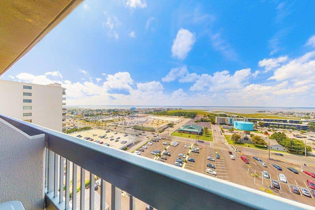Blick vom Balkon auf einen Parkplatz und Gebäude, mit blauem Himmel und Wolken.