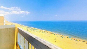 Un balcón con vista a una playa con sombrillas y gente.