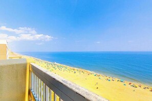 Ein Balkon mit Blick auf einen Strand mit Sonnenschirmen und Menschen.