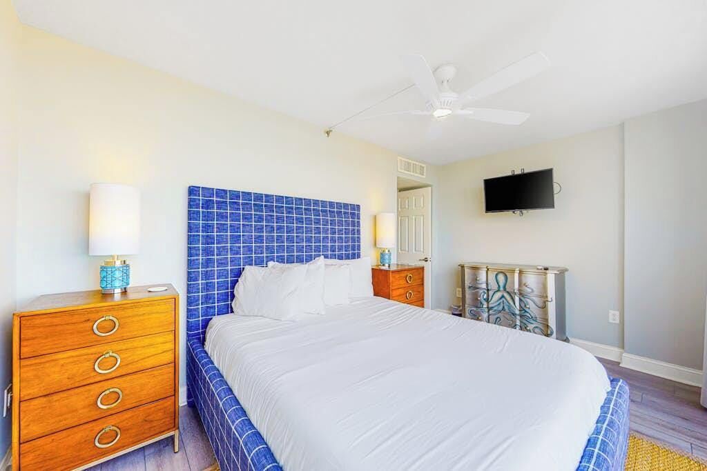 A bedroom with a bed, a dresser, a television, and a ceiling fan.