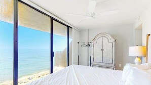 Habitación de hotel con cama, ventilador de techo, armario y vista a la playa.